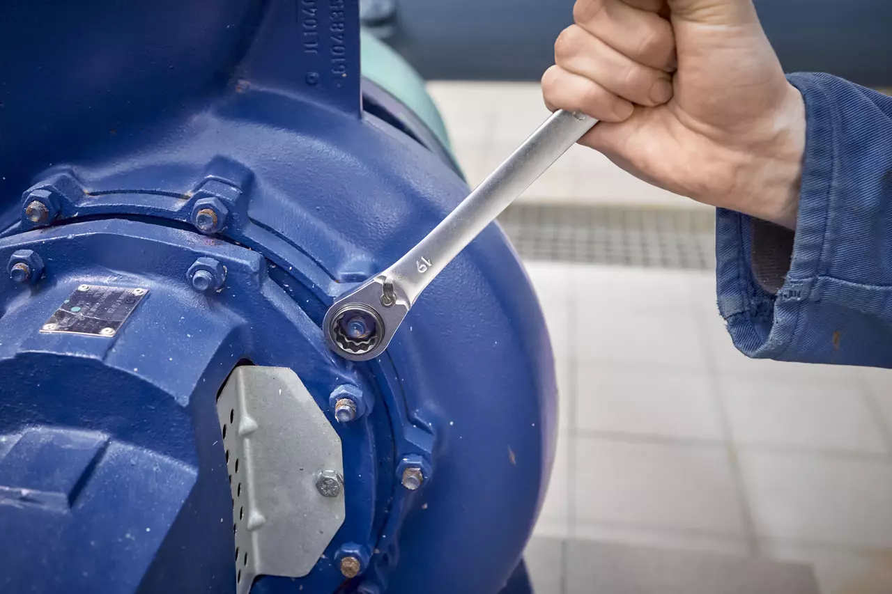 A person using a ratchet wrench to tighten a bolt on a large blue machine.