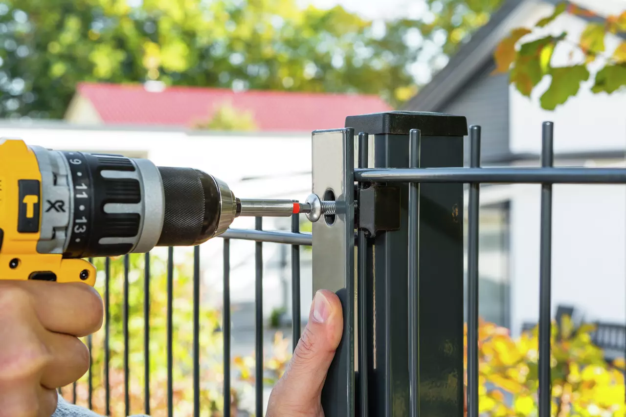 Person using a yellow drill on a metal fence post outdoors.