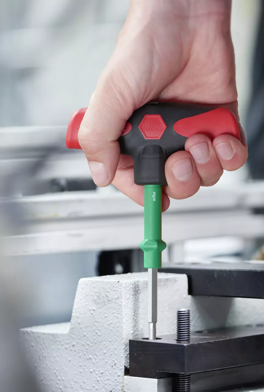 Hand using T-handle screwdriver with green shaft on metal object