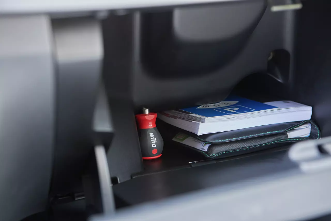 Red and black screwdriver in a glovebox with a book and a folder.