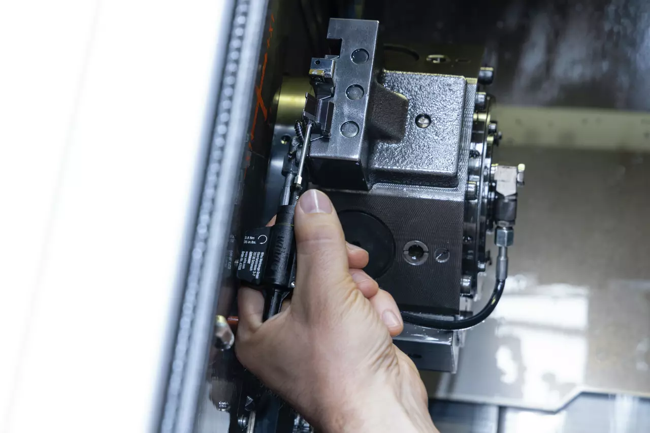 Iemand gebruikt een gereedschap op een metalen onderdeel in een CNC-machine.