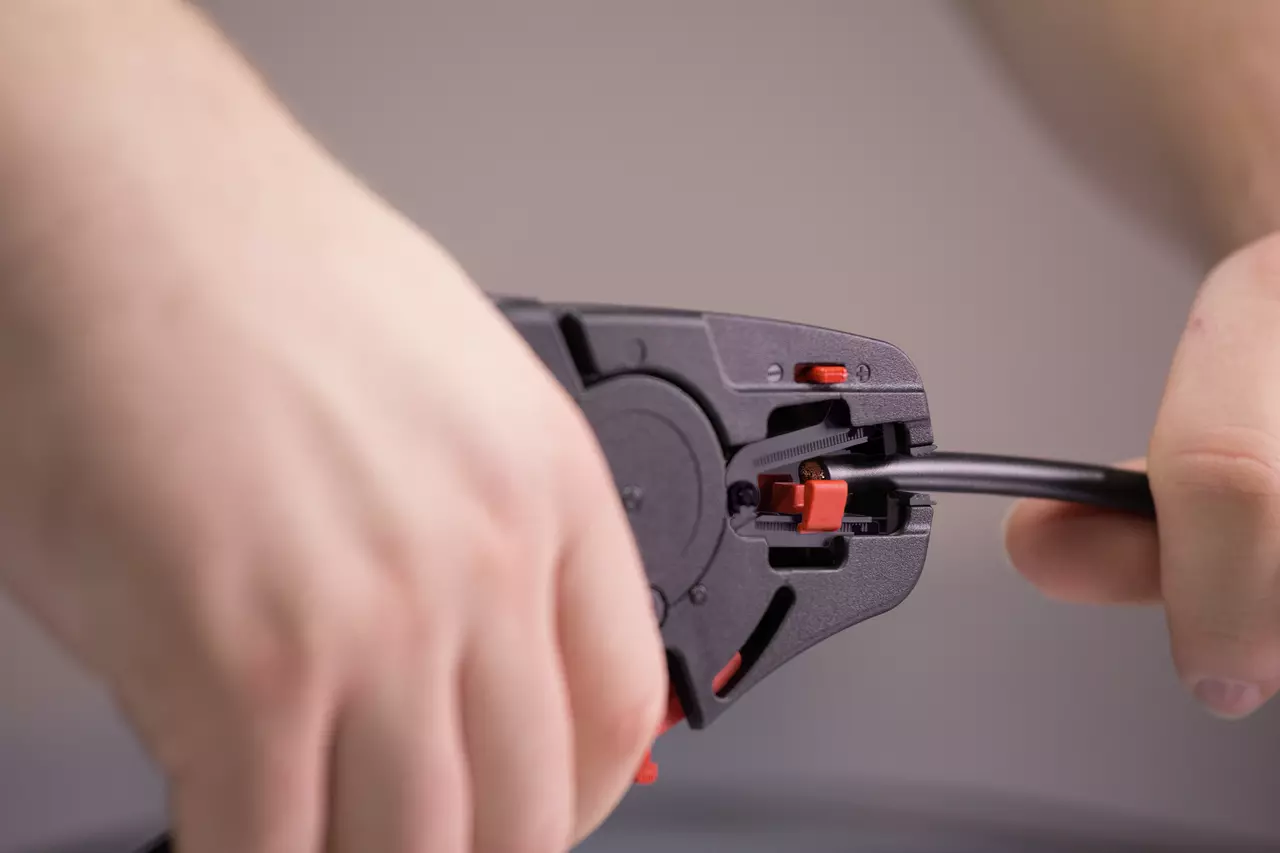 Hands using an automatic wire stripper on a black cable.