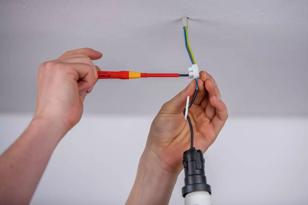 Person using a red insulated screwdriver to work on ceiling electrical wires.