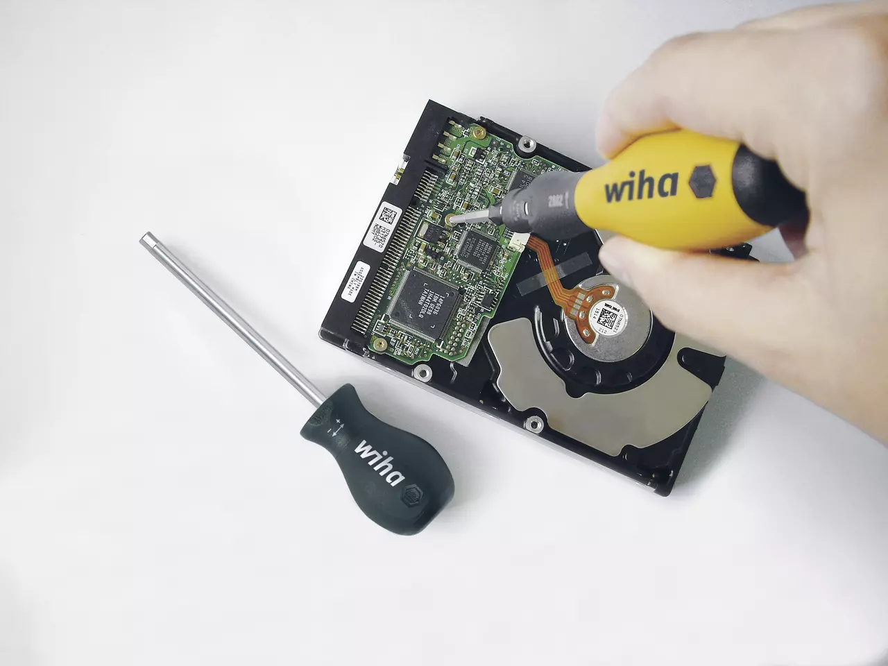 A person uses a yellow-handled screwdriver on a hard drive