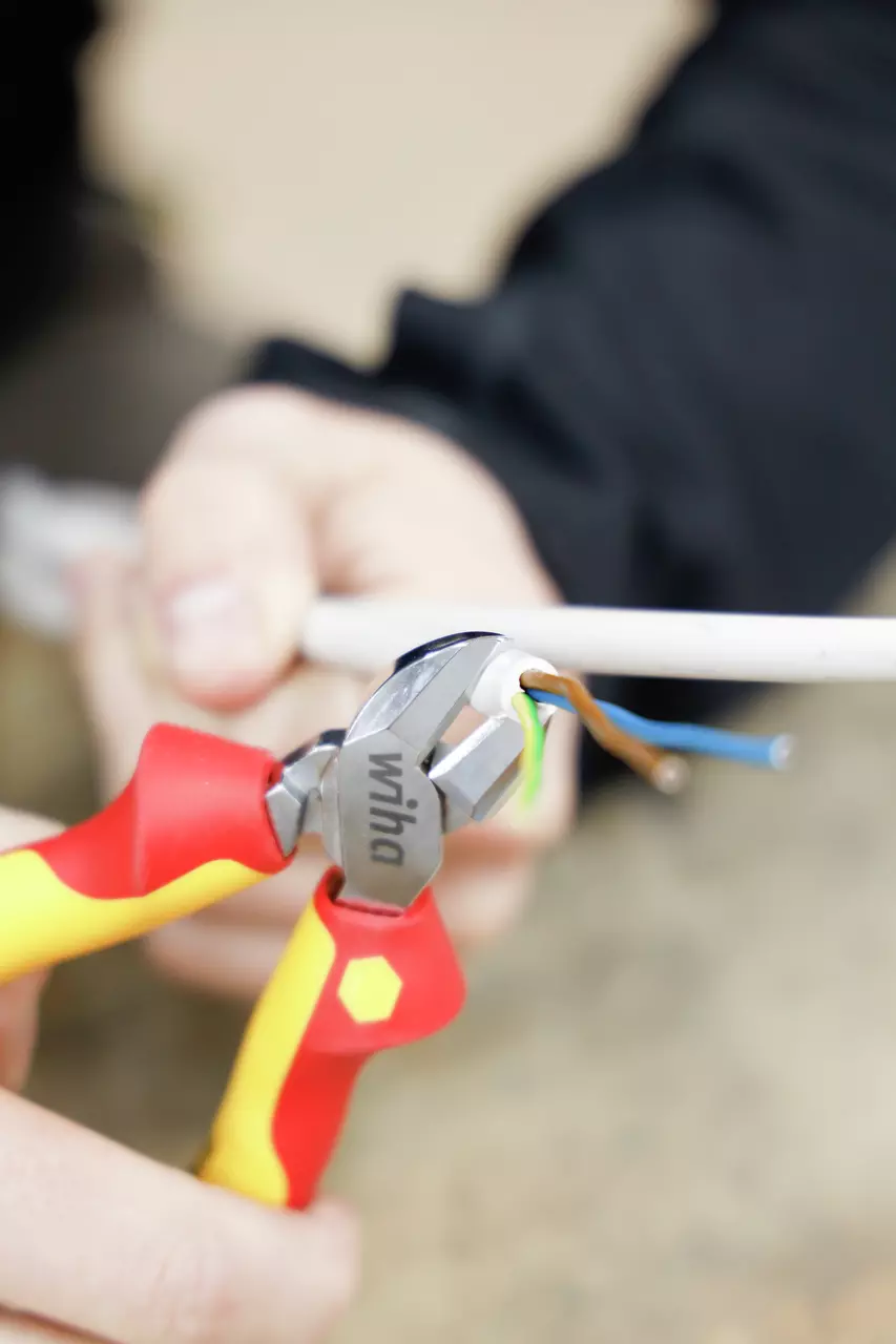Person using insulated side cutters on electrical cable