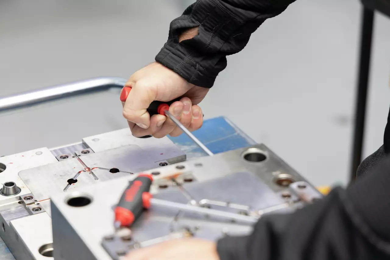 A person uses a red-handled tool on a metal surface