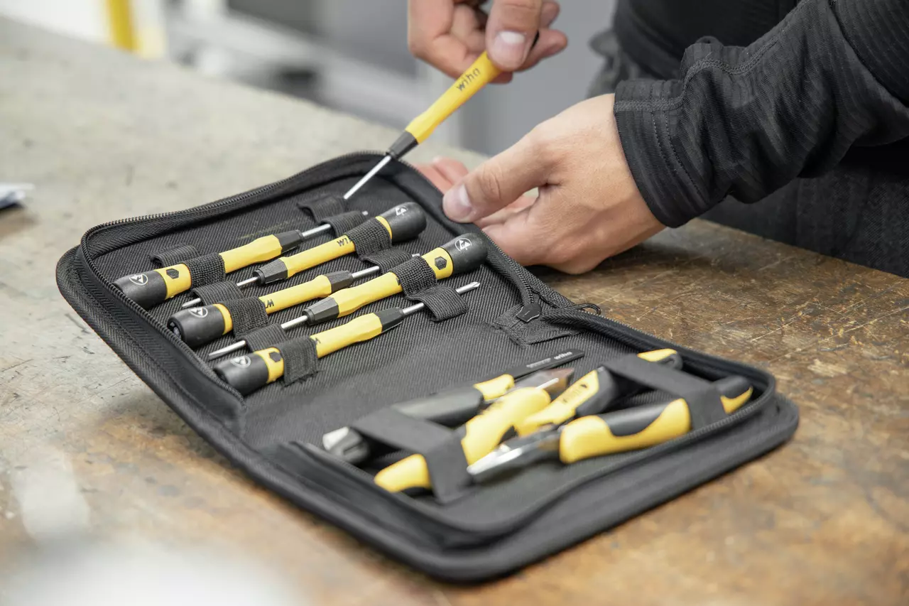 A person using a yellow-handled screwdriver from a tool set on a table.