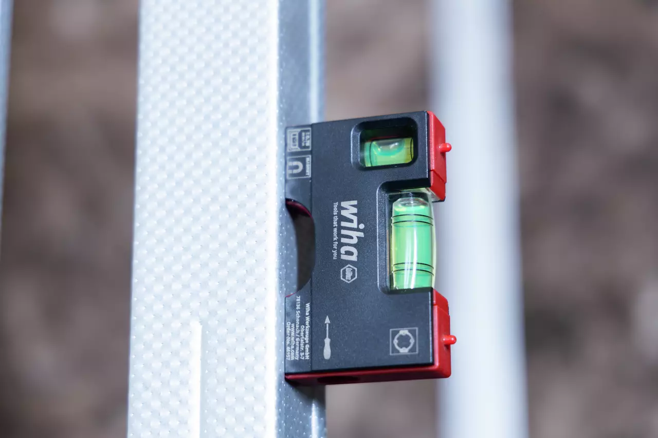 Pocket level with magnet on metal surface, black and red housing with green liquid vials.