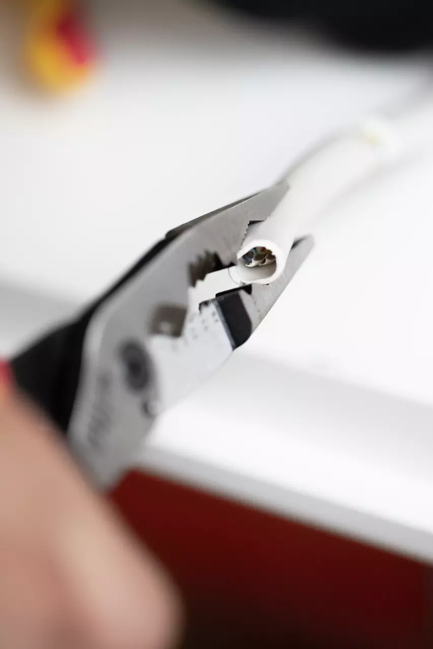 Tang grijpt een witte kabel, toont interne draden.