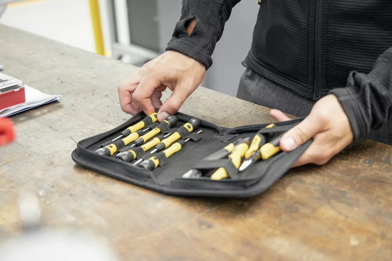 Person holding a yellow and black tool set in a black case on a workbench.