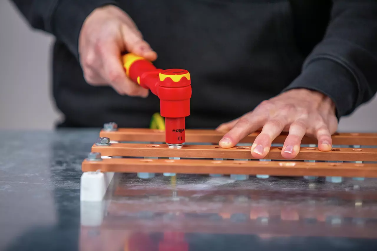 A person using a red and yellow insulated torque wrench on copper bus bars.