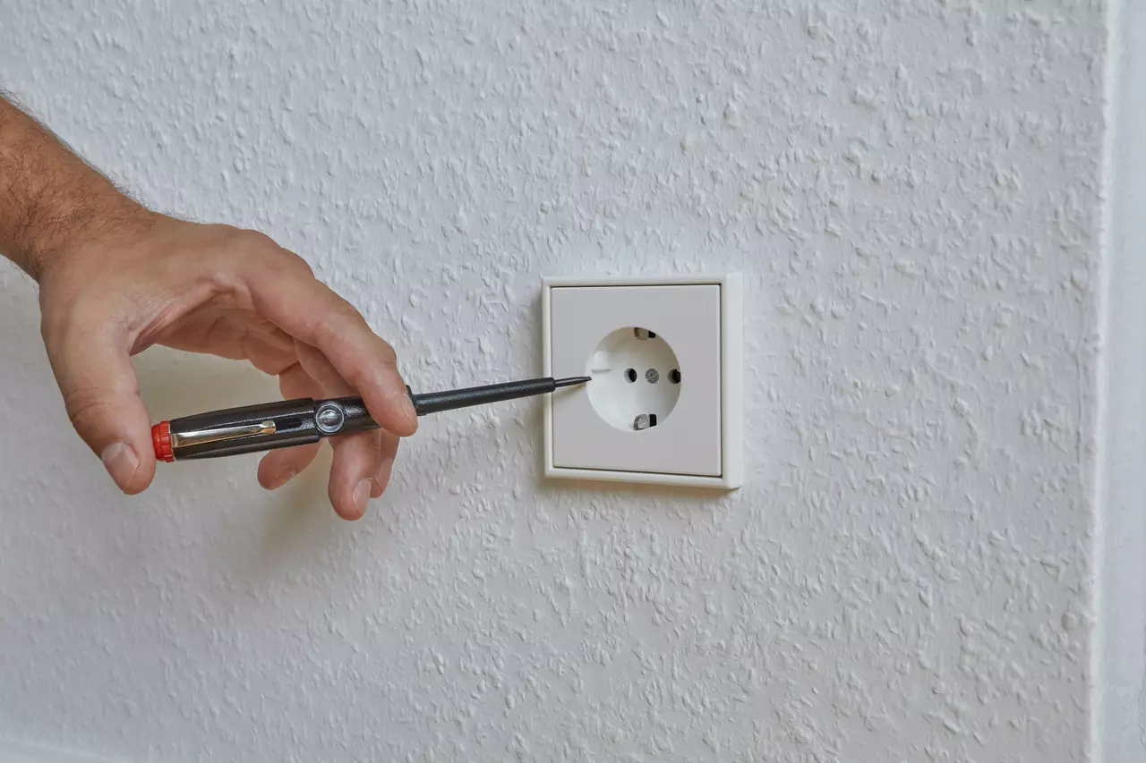 A person using a voltage tester on a wall socket.