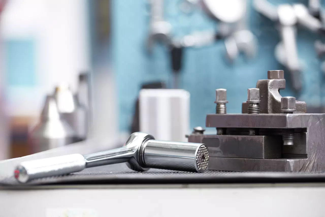 A metal ratchet wrench next to a metal vice on a workbench.