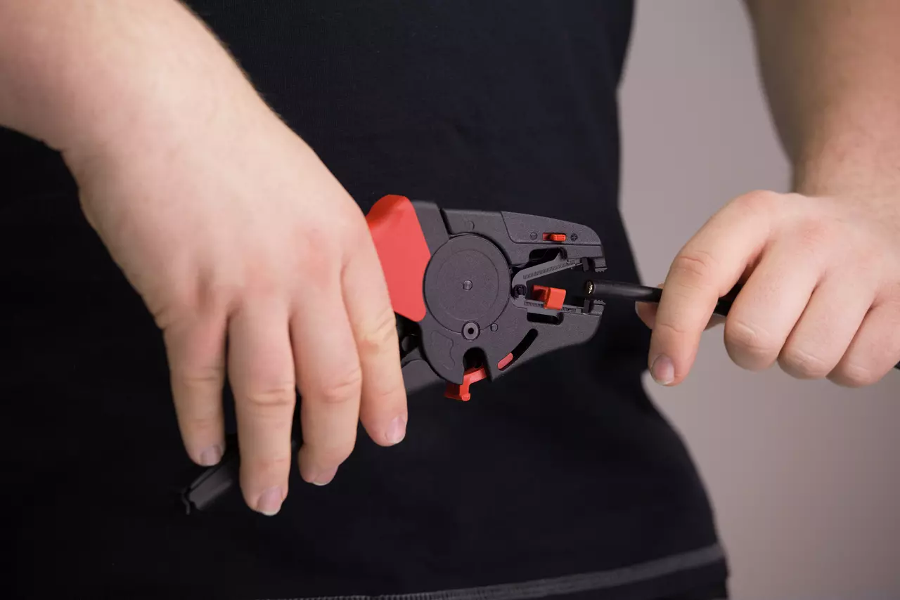 A person using an automatic wire stripper on a black cable.
