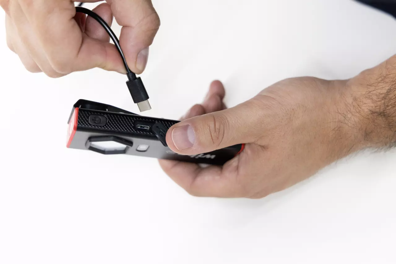 Eine Person verbindet ein Ladekabel mit einem schwarzen Handgerät.