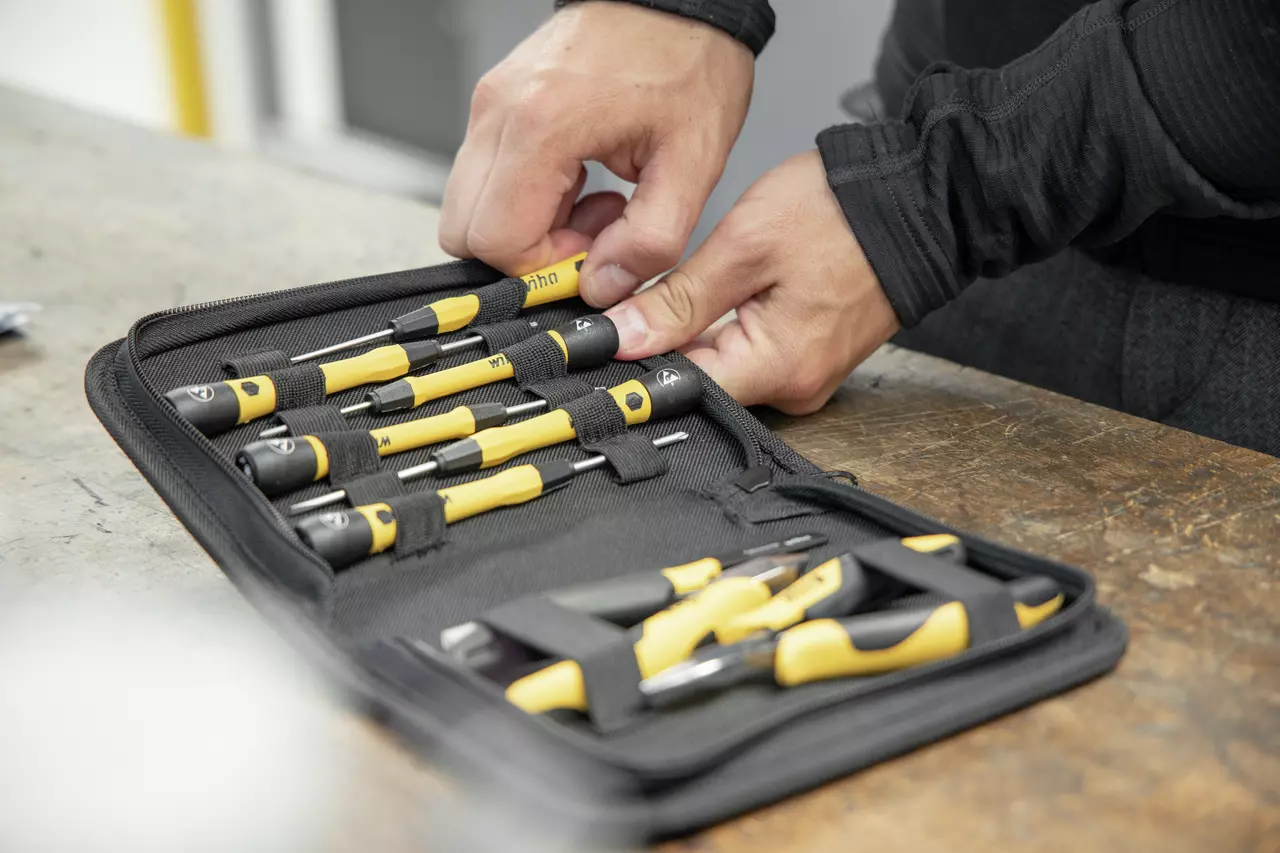 Person organizing a tool set with yellow and black screwdrivers in a black case on a workbench.