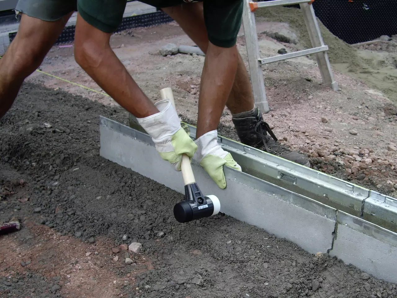 Person using a rubber mallet to adjust a concrete slab on a construction site.
