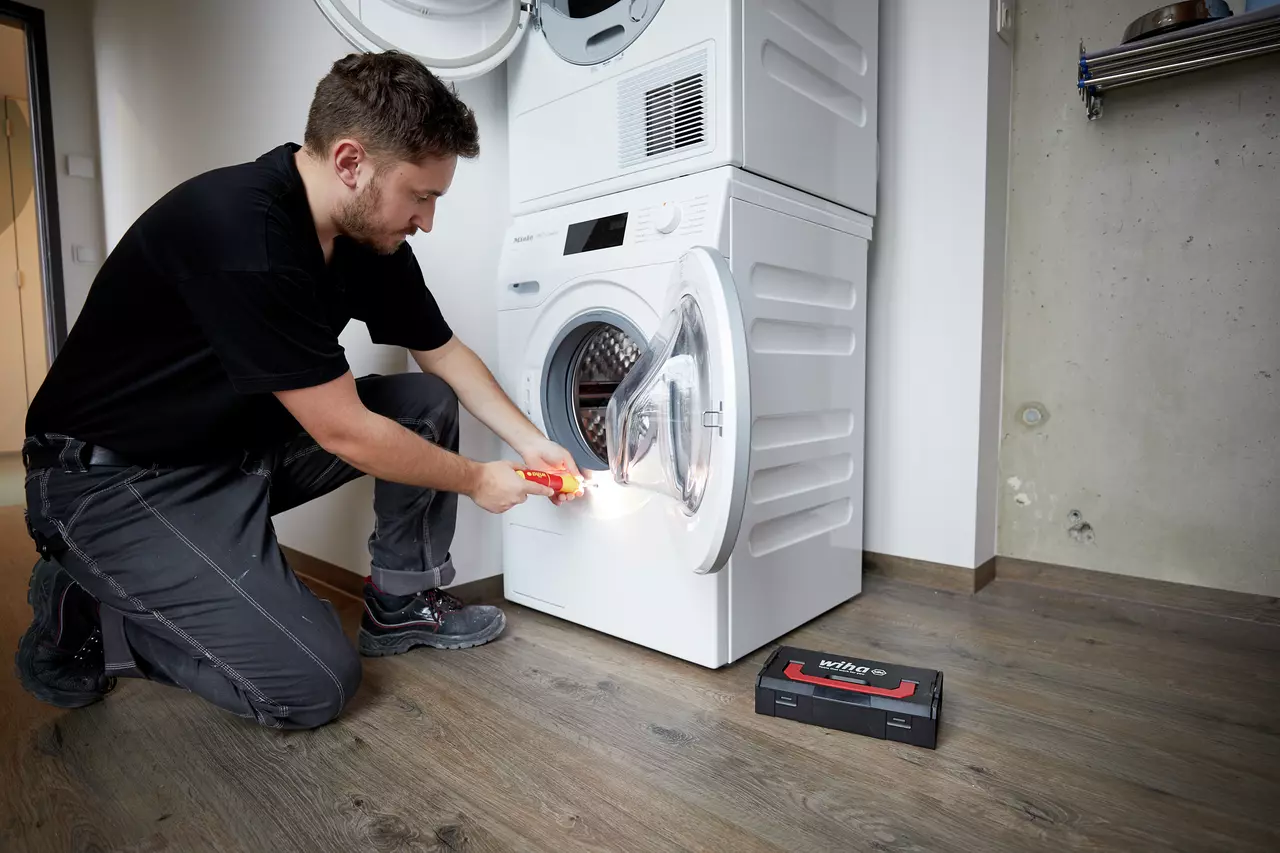 A person using an electric screwdriver to work on a washing machine door.