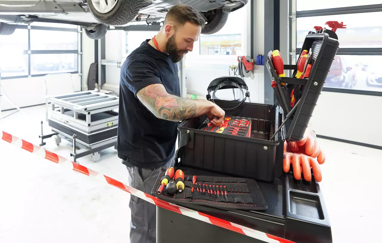 A person working with tools in a garage, organizing a toolbox on a cart.