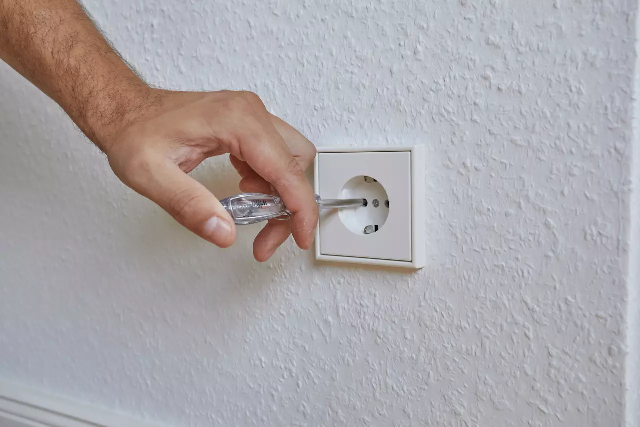 Hand using a voltage tester on a wall power socket.