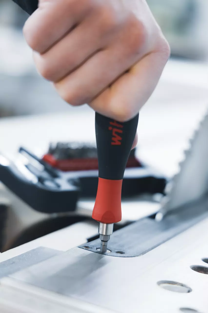 Person using a screwdriver to fasten a screw on a metal surface.