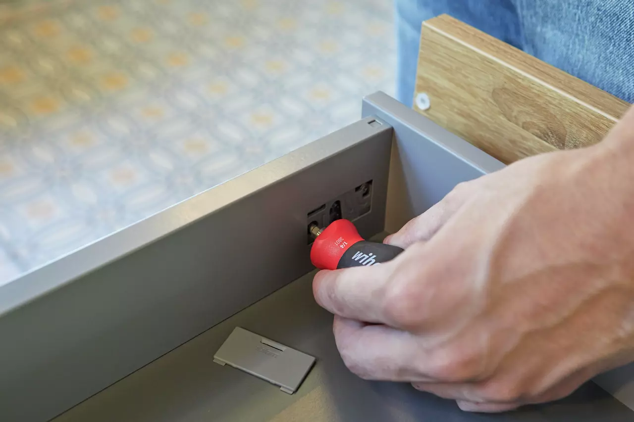 Person using a red-handled screwdriver on a drawer