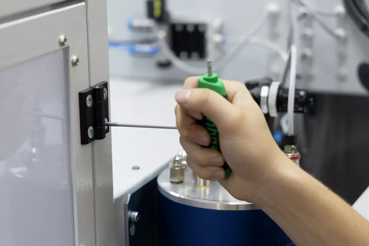 A person using a green-handled hex key on a metal hinge