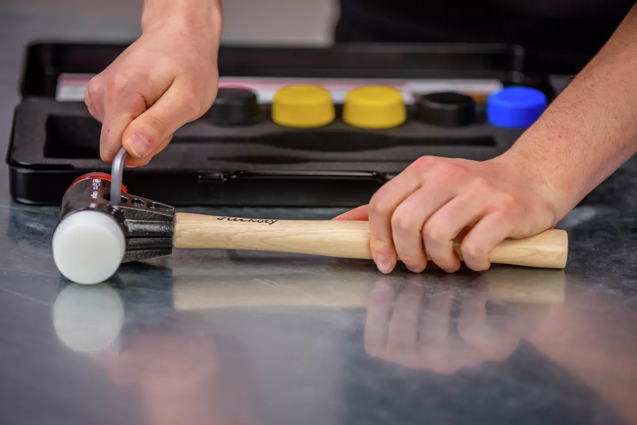 Person holding a mallet with a wooden handle, alongside interchangeable rubber caps in a case.