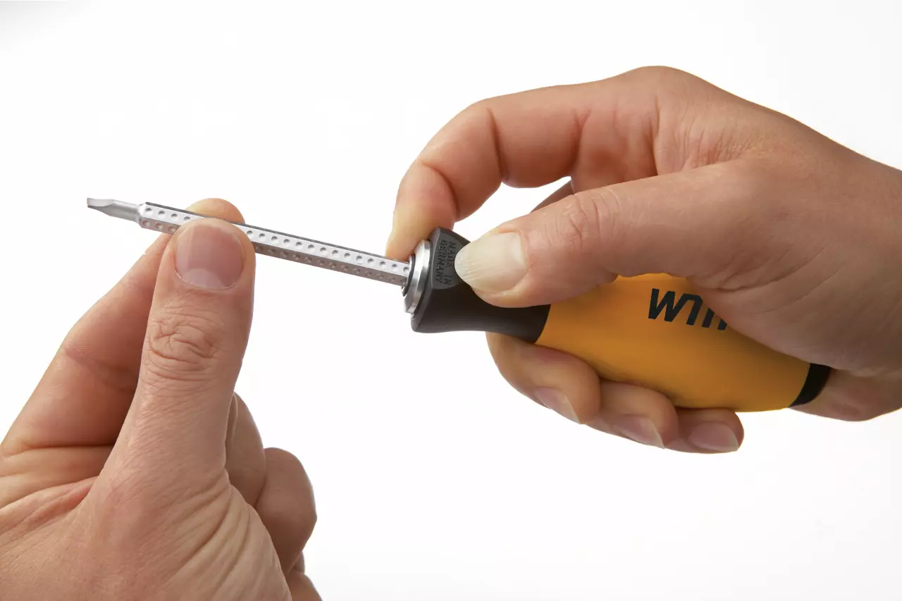 Hands holding a screwdriver with a yellow handle and a metal bit being inserted or removed.