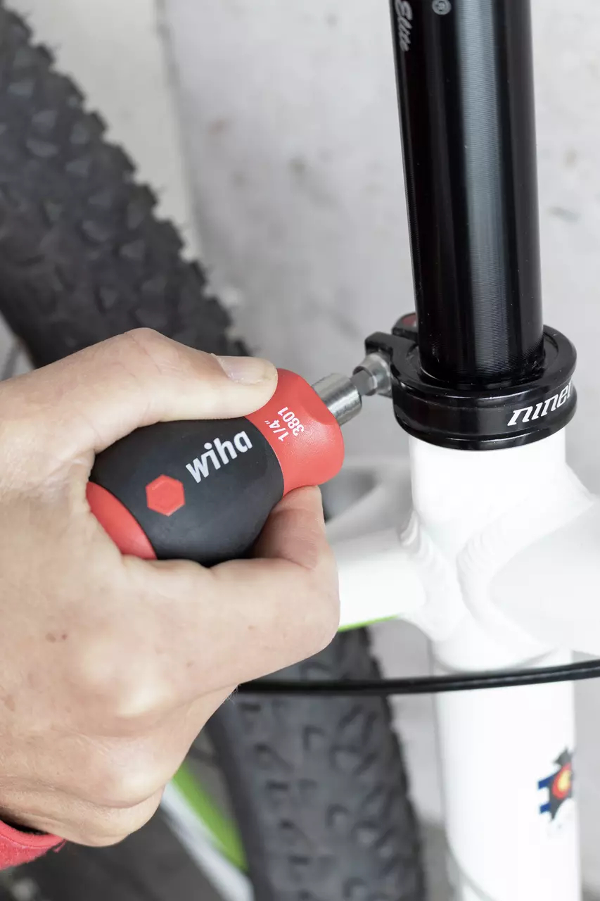 A person uses a red and black screwdriver on a bicycle seat post clamp.