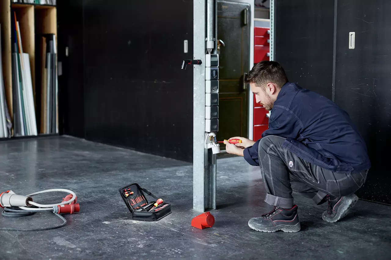 A man repairs an outlet with a screwdriver, tool kit on the floor