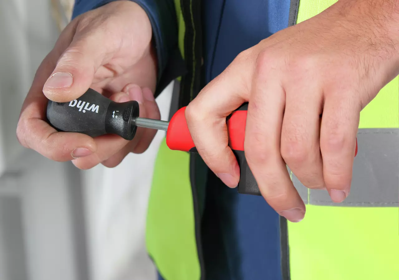 Person using a red and black screwdriver on a tool with a black handle.