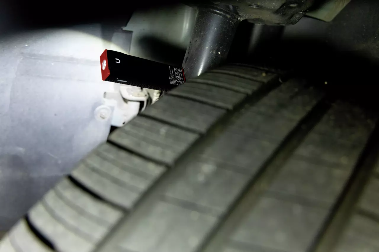 Close-up of a black and red flashlight illuminating a car tire