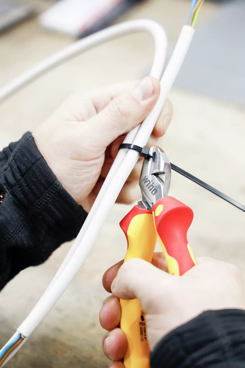 Hands using side cutters to cut a cable tie around white cables.