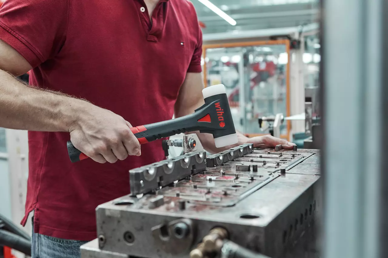 Eine Person benutzt einen Schonhammer auf einer Metalloberfläche in einer industriellen Umgebung.