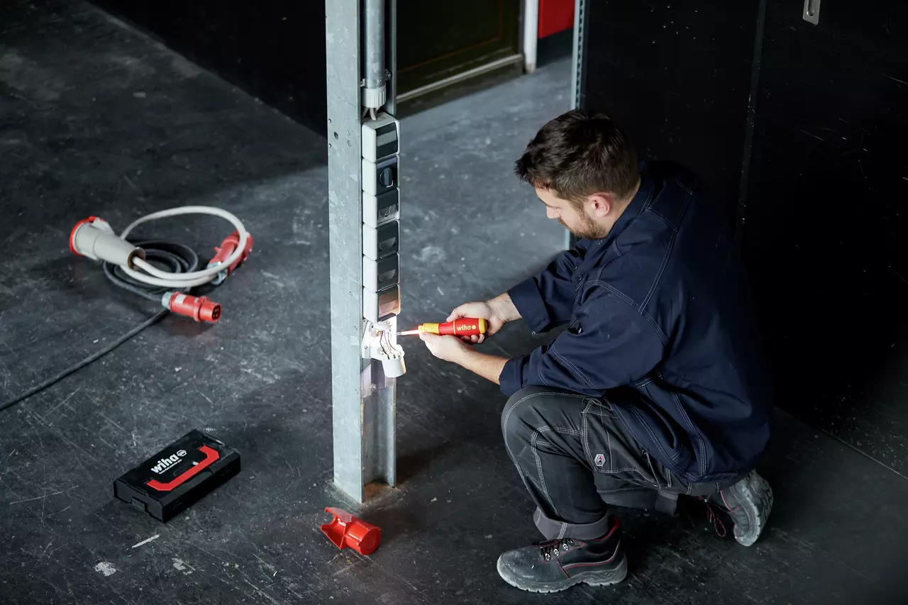 A man works with an electric screwdriver on an outlet on a metal post.