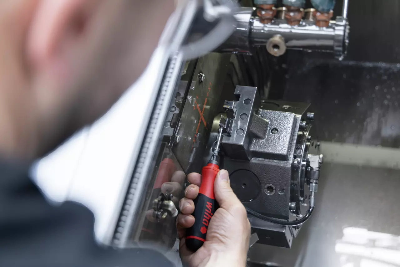Person using an electric screwdriver on a metal machine part in a workshop.