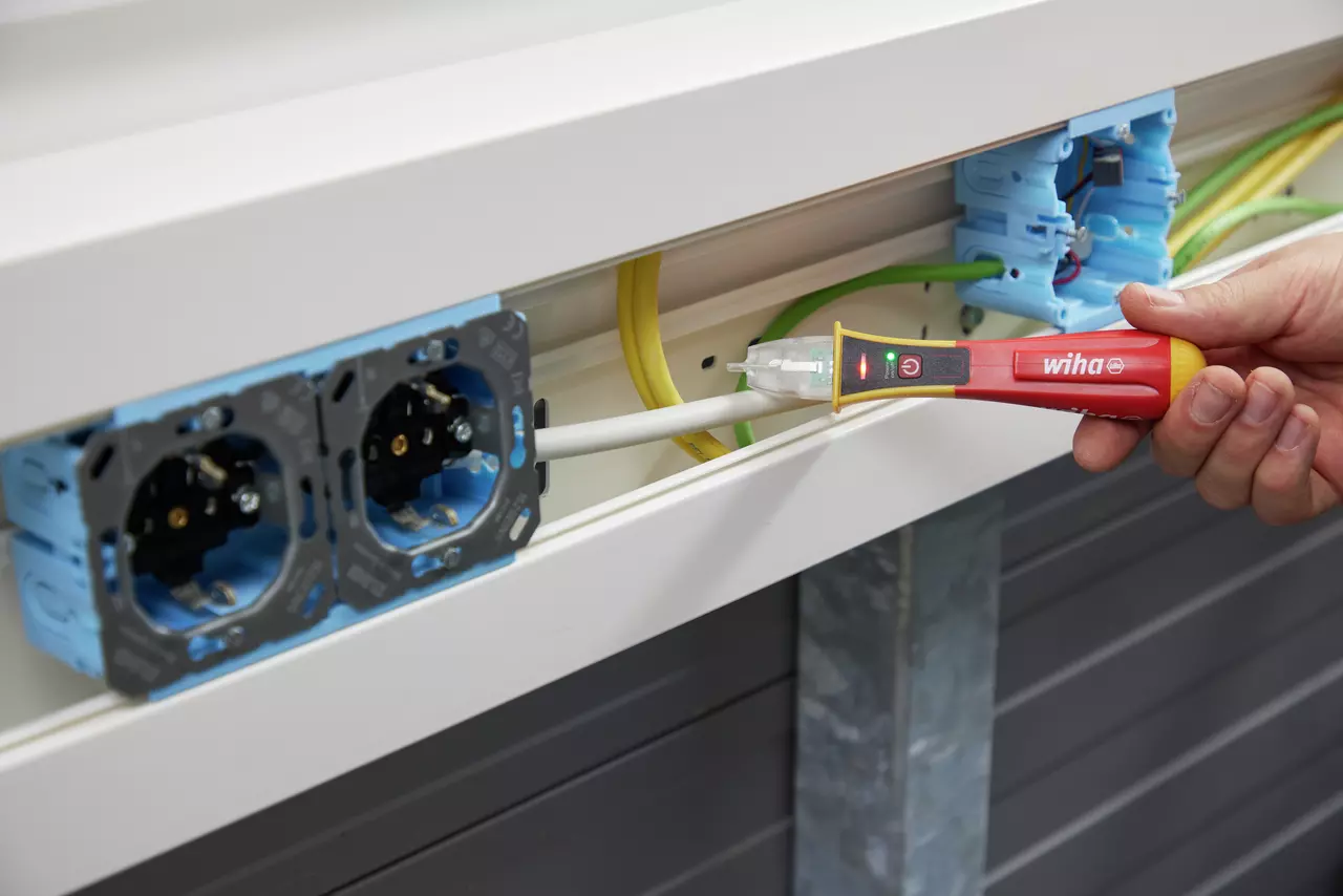 A person using a non-contact voltage detector on a white cable near electrical sockets.