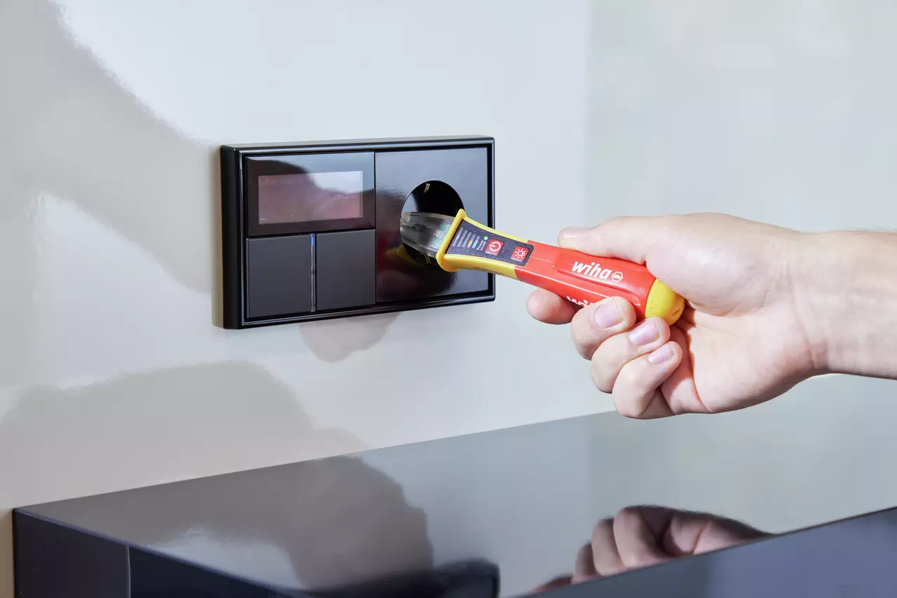 A hand using a non-contact voltage detector on a wall socket.