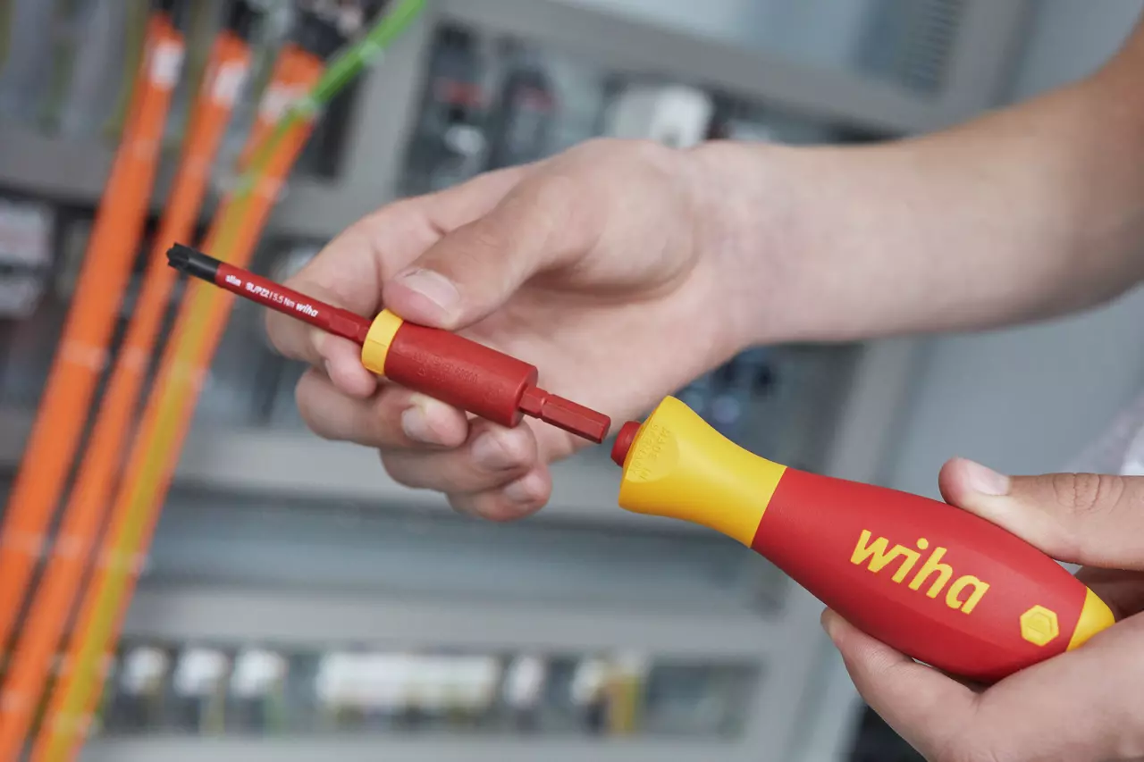 Person assembling a red and yellow electric screwdriver in front of an electrical panel.