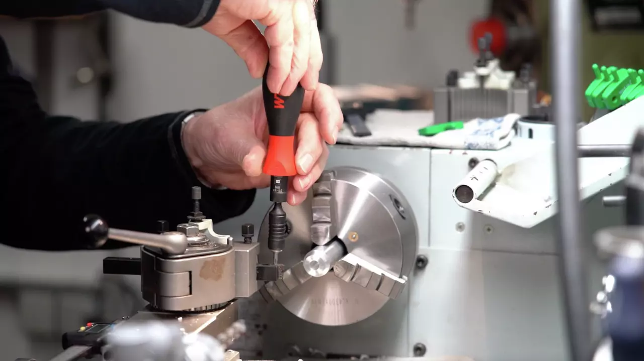 A person uses a torque screwdriver on a metal lathe machine part.