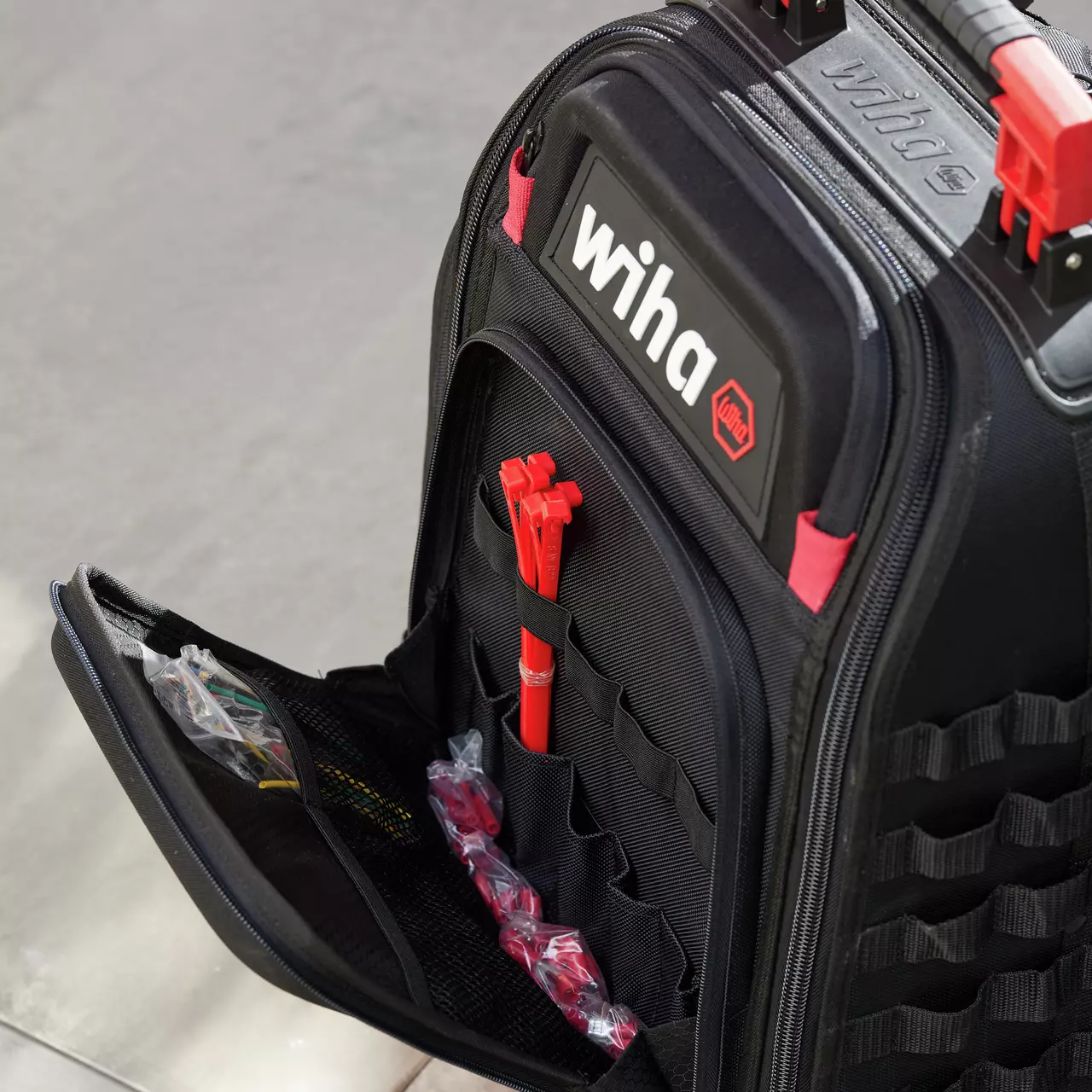Black tool backpack with red accents, open to show tool compartments and storage pockets.