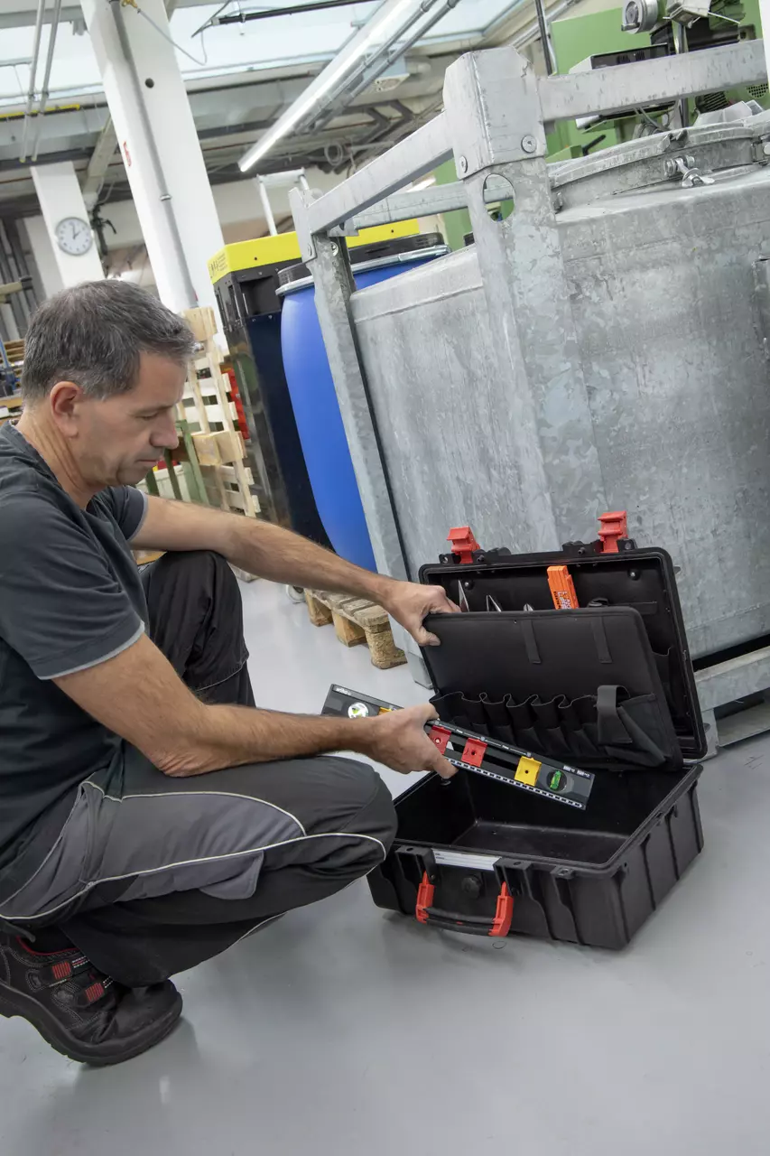 A person organizing tools in a black tool case, holding a level
