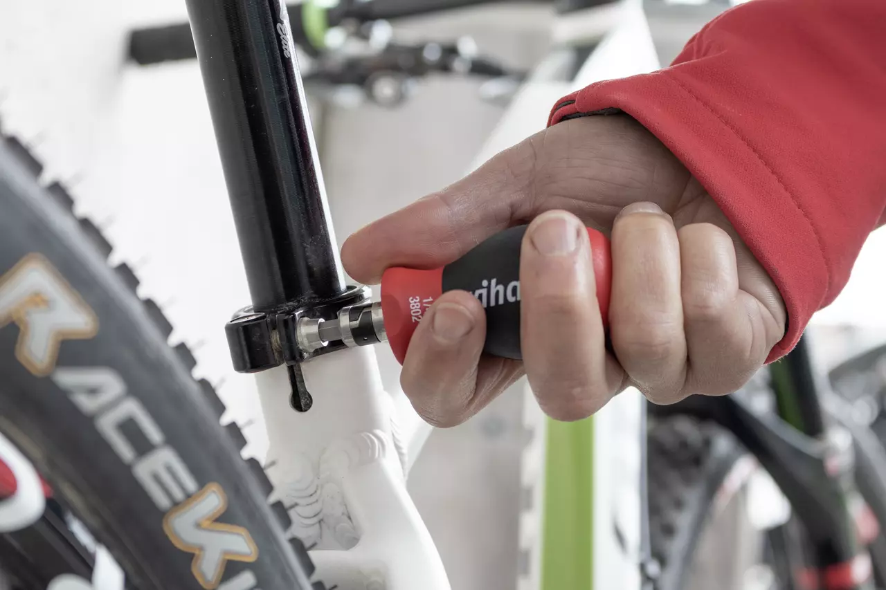 Hand gebruikt een rood-zwarte schroevendraaier om de zadelpen van de fiets af te stellen.