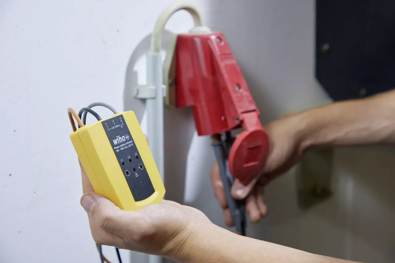Person holding a yellow rotational field indicator near a red electrical connector.