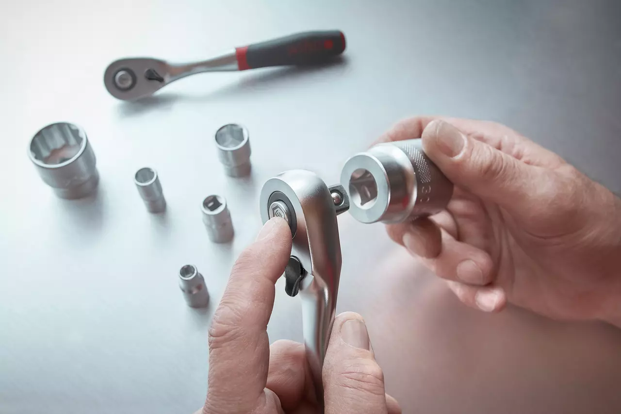 Hands using a ratchet wrench with socket attachments on a metallic surface.
