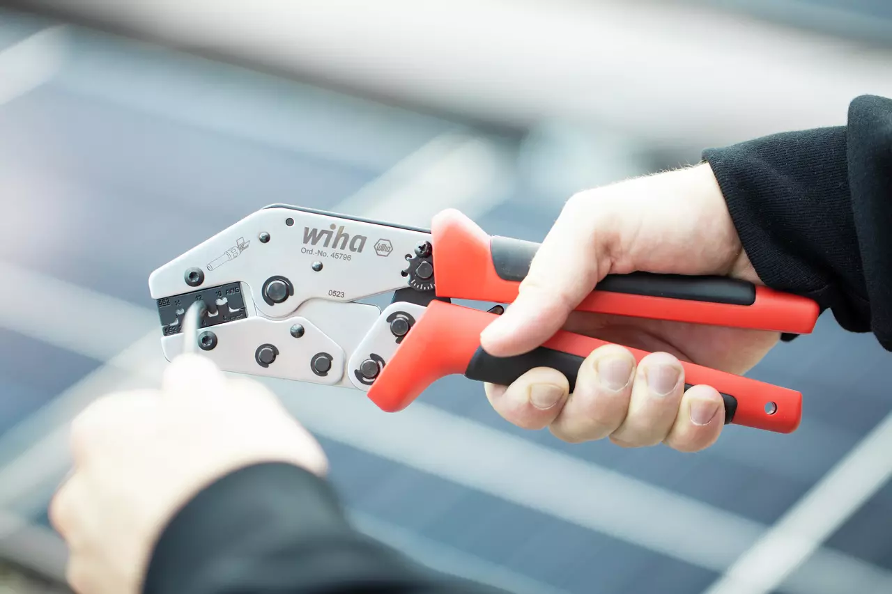 Hånd holder en crimpetang med røde og sorte håndtag, brugt til elektrisk arbejde.
