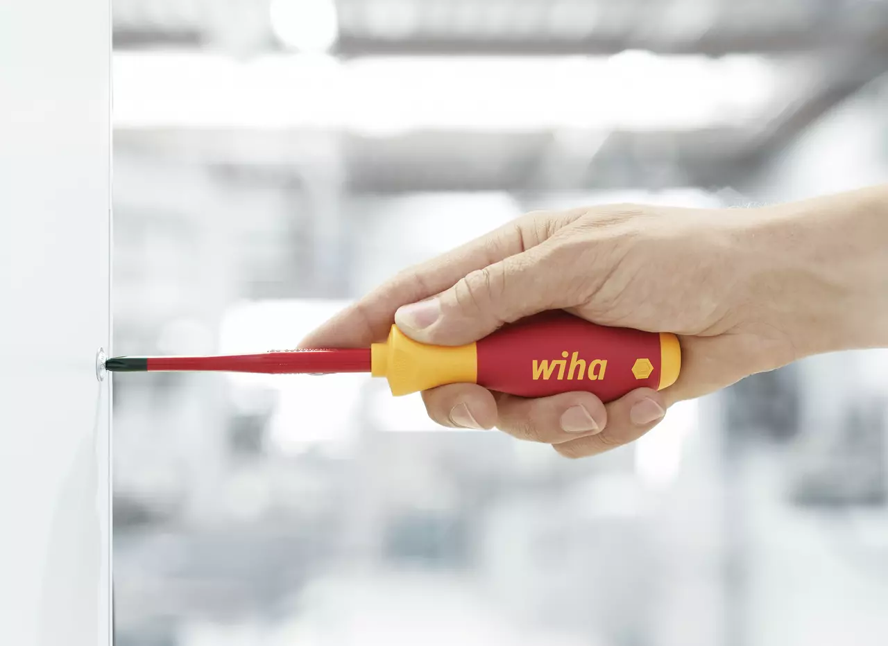 A hand using a red and yellow insulated screwdriver on a screw