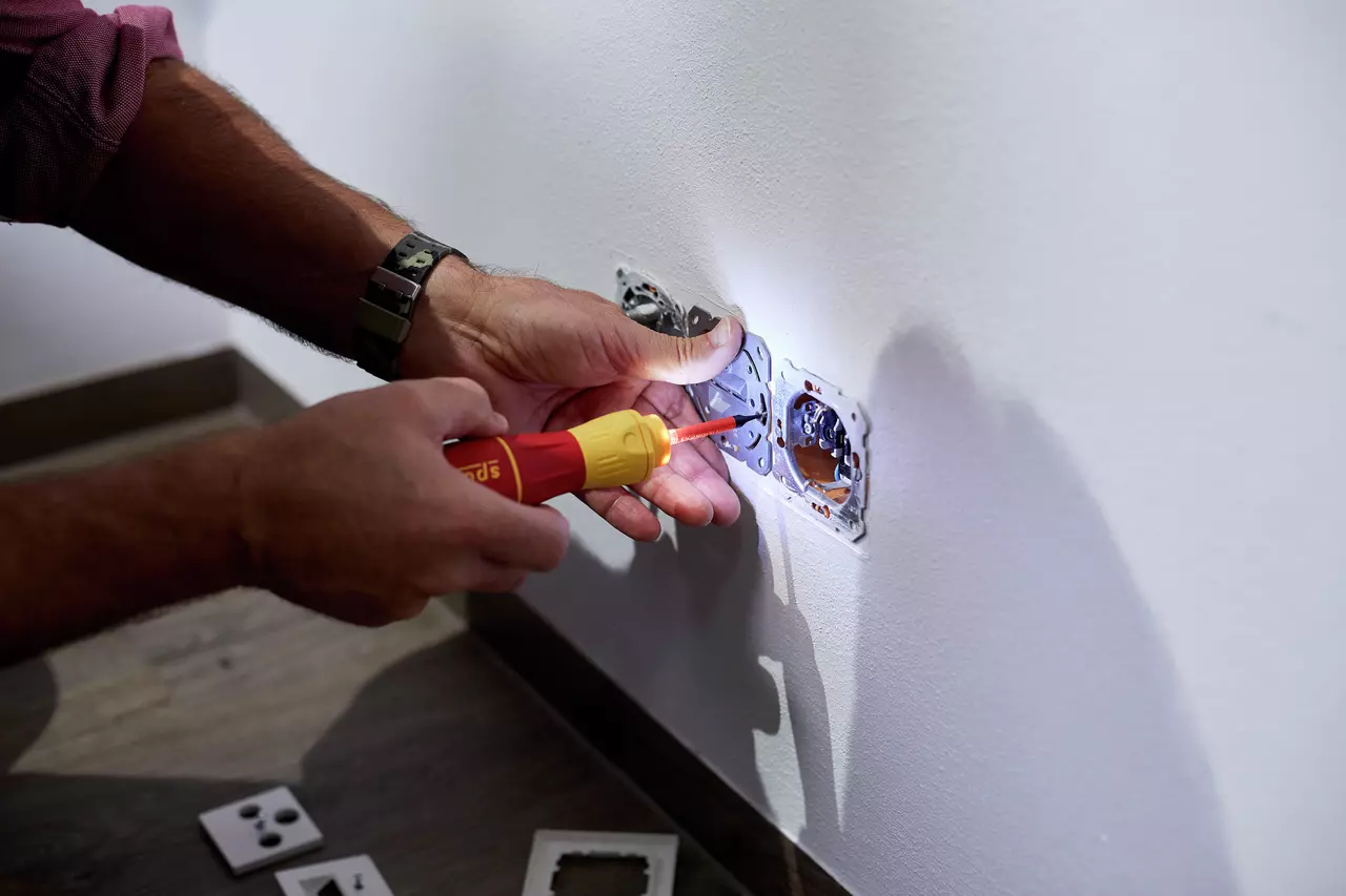 Person using an electric screwdriver on a wall socket. The tool is red and yellow.