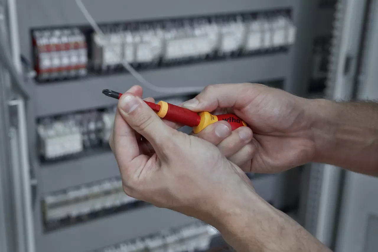 Person using a red and yellow electric screwdriver near an electrical panel.